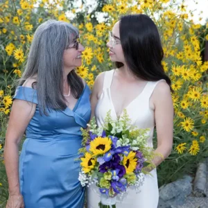A bride holding a bouquet smiles at her mother in this touching wedding photo
