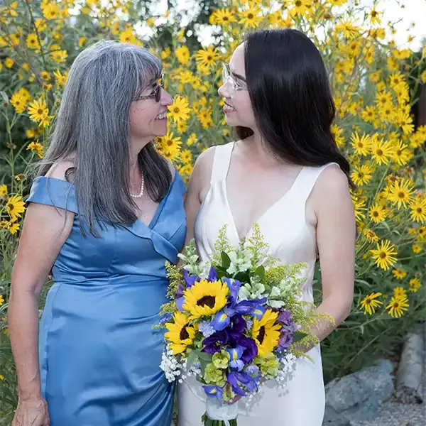 A bride holding a bouquet smiles at her mother in this touching wedding photo