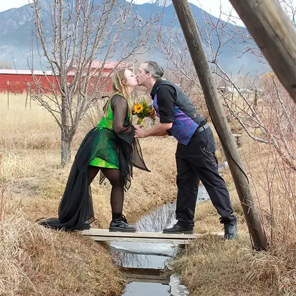 newly married couple kiss each other standing on a bridge over a little stream