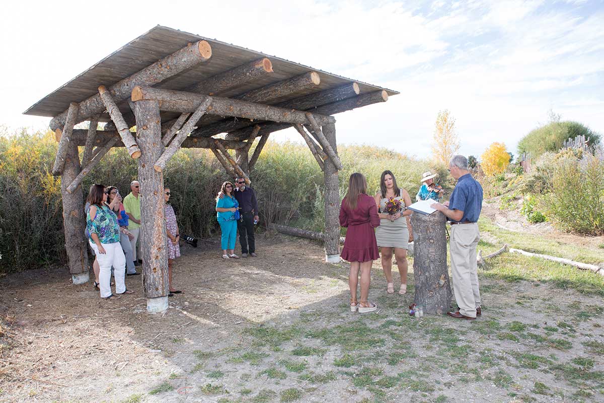 Wedding guests gathered underneath a shelter watching a couple get married in an outdoor micro wedding venue.